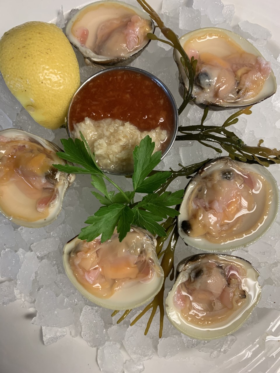 Six Little Neck Clams with horseradish and cocktail sauce garnished with a wedge of lemon all over ice