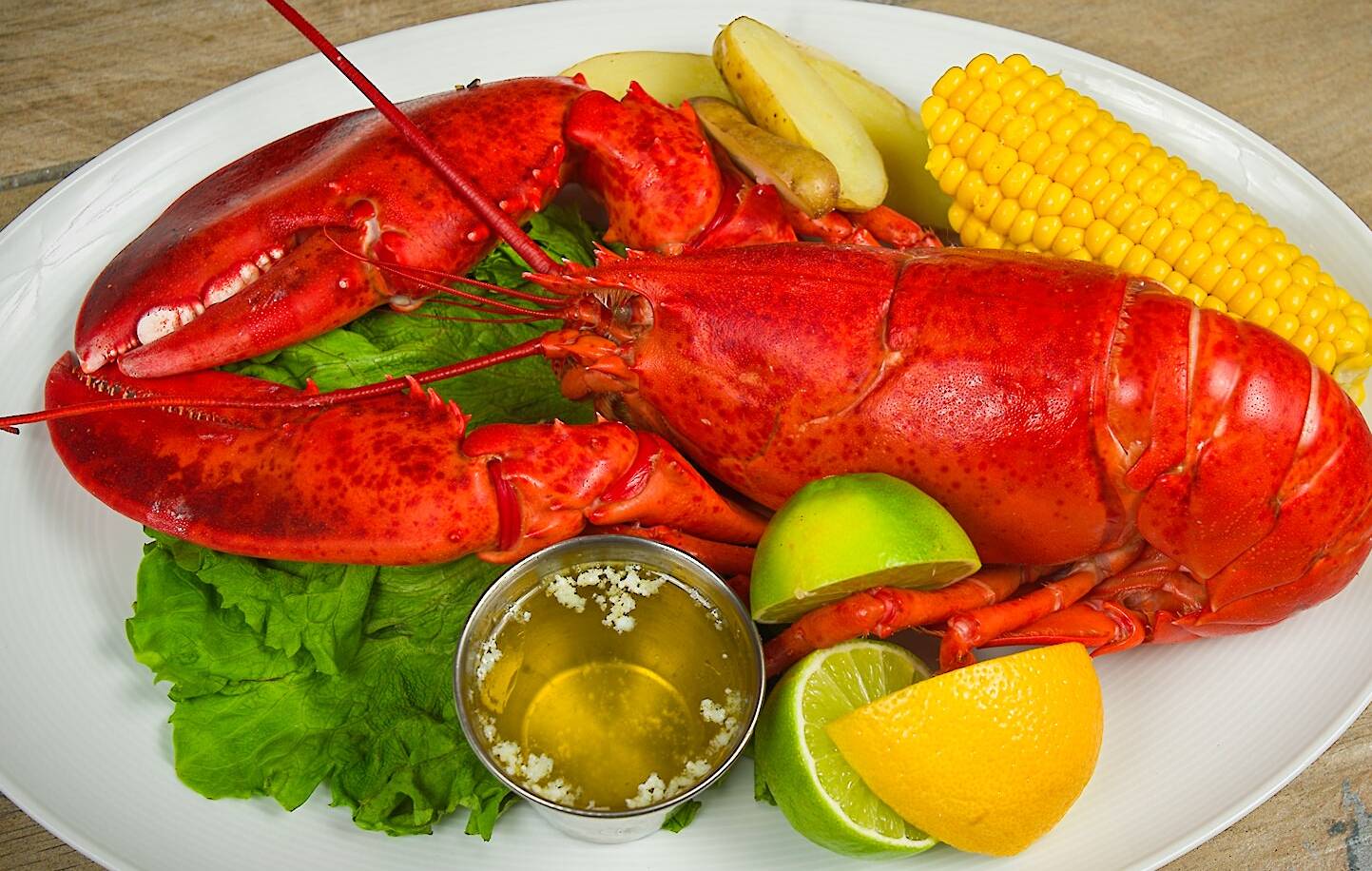 Whole Lobster served with a side of corn on the cob and fingerling potatoes, melted butter and lemon wedges