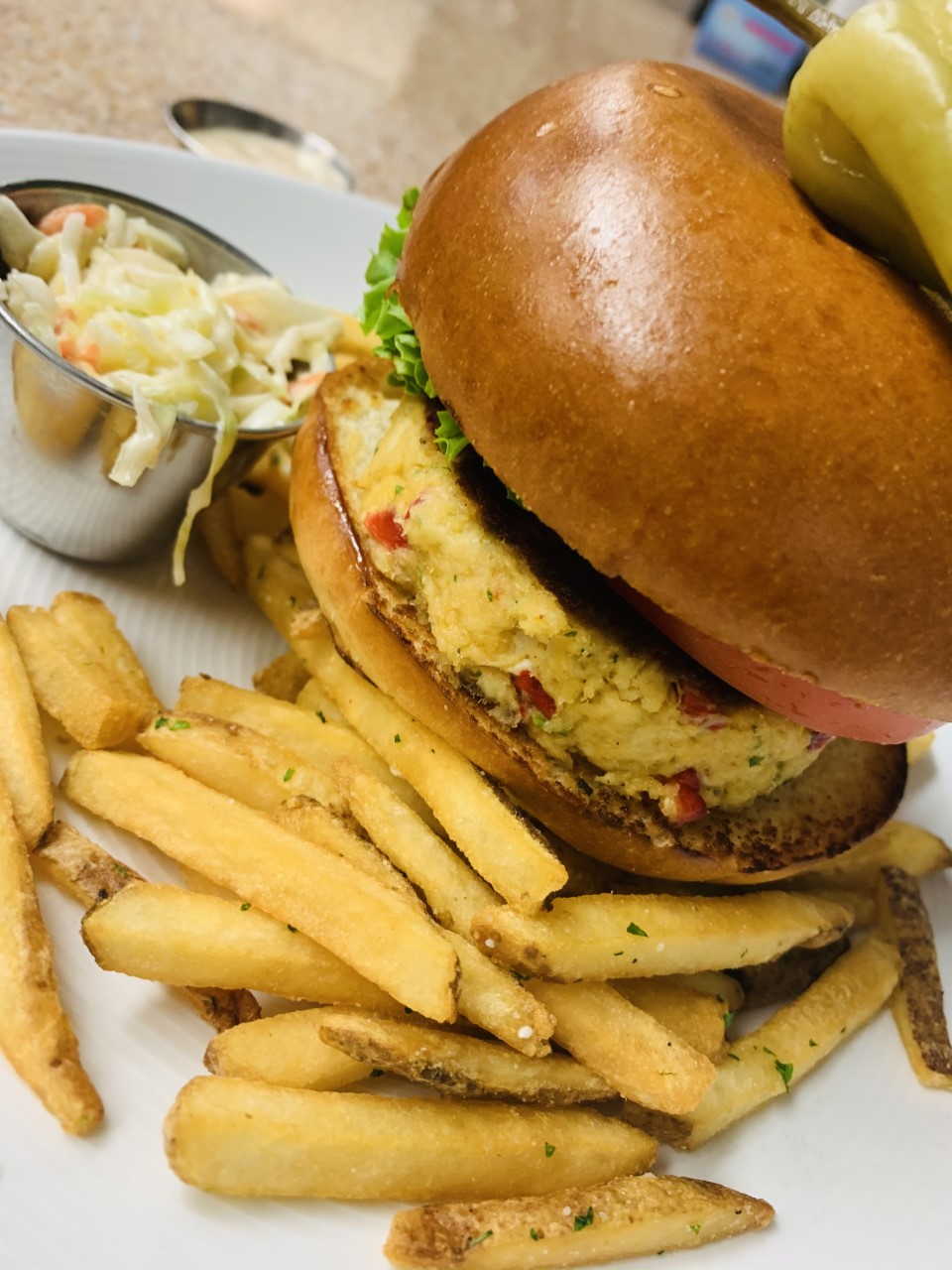 Crabcake burger on a bun with lettuce and tomato served with hand cut fries and cole slaw