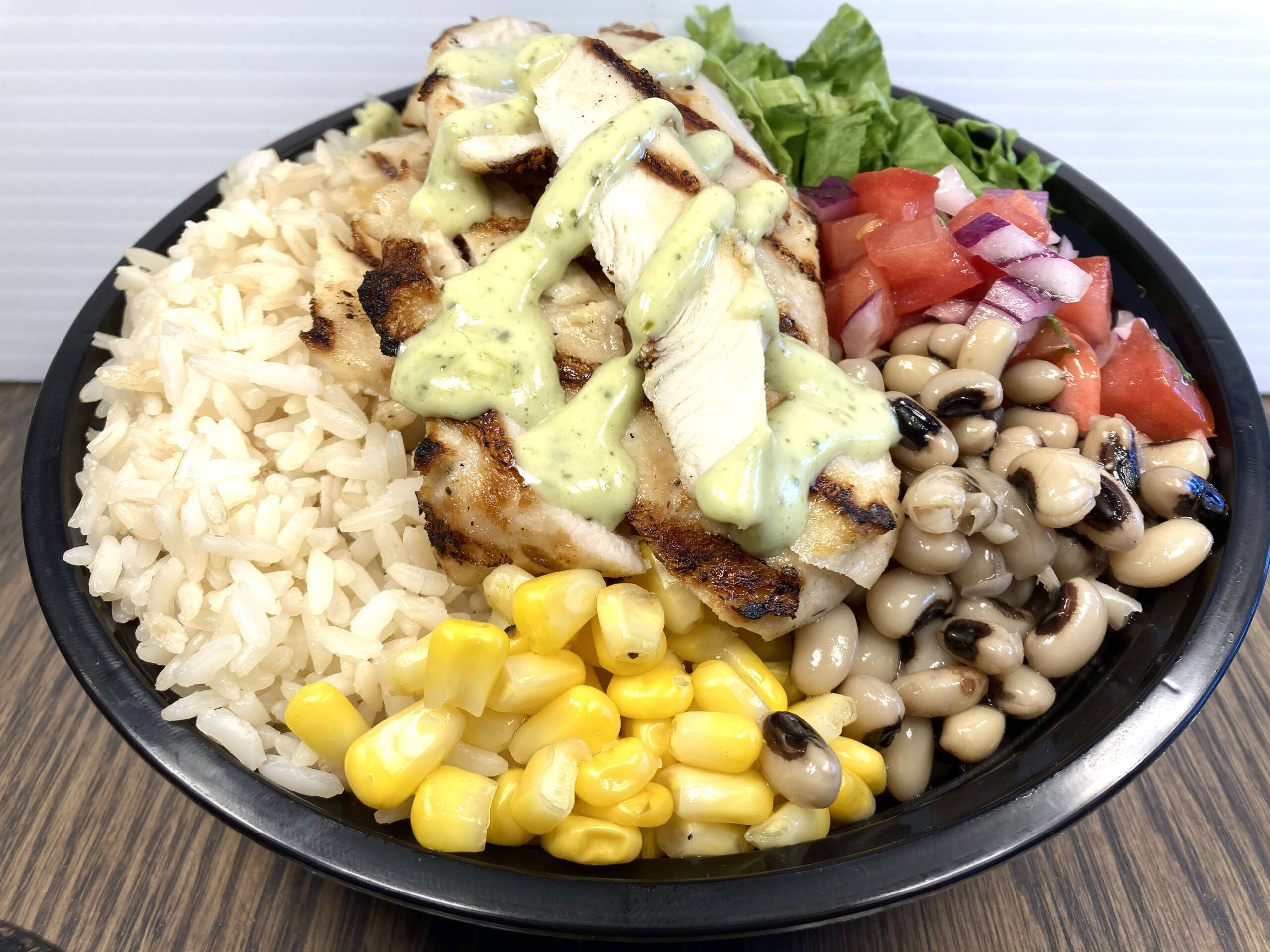 Grilled chicken bowl served with Mediterranean Rice, Romaine Lettuce, Corn, Black Eyed Beans, Diced Tomato, Diced Red Onions, Cilantro, and Fresh Herb & Cream Sauce